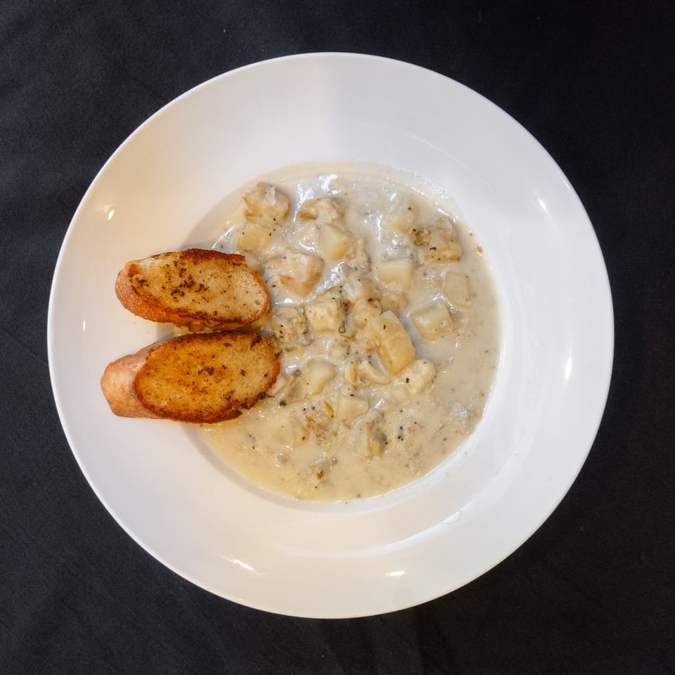 Creamy clam chowder with potatoes and two slices of toasted garlic bread in a white bowl.