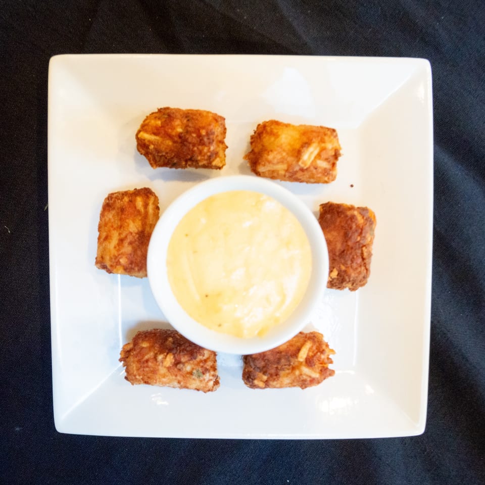 Six golden-brown fried appetizers arranged around a small white bowl of creamy yellow dipping sauce.