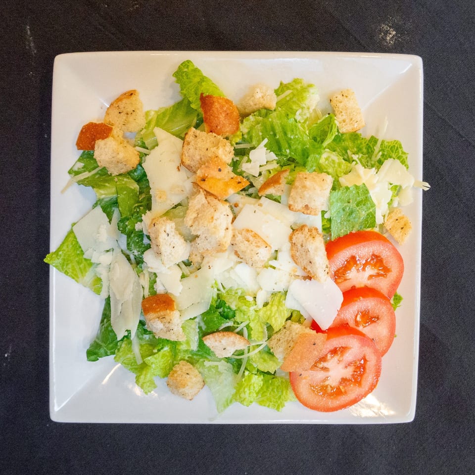 Overhead view of a Caesar salad with romaine lettuce, croutons, parmesan cheese, and tomato slices.