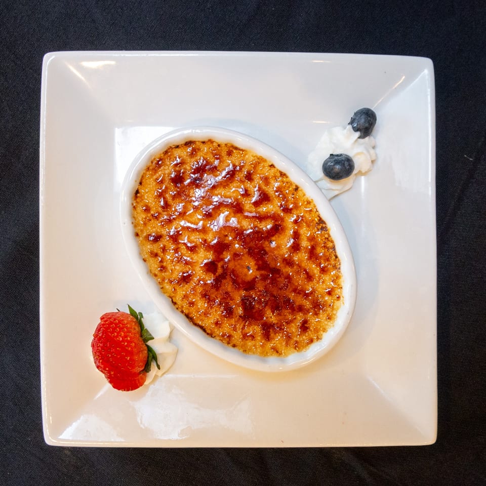 Crème brûlée in an oval dish, garnished with whipped cream, a strawberry, and blueberries.