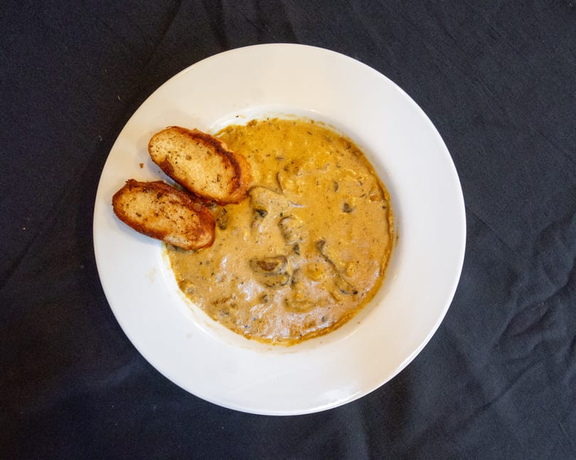 Creamy mushroom soup with two slices of toasted bread on a white plate against a dark background.