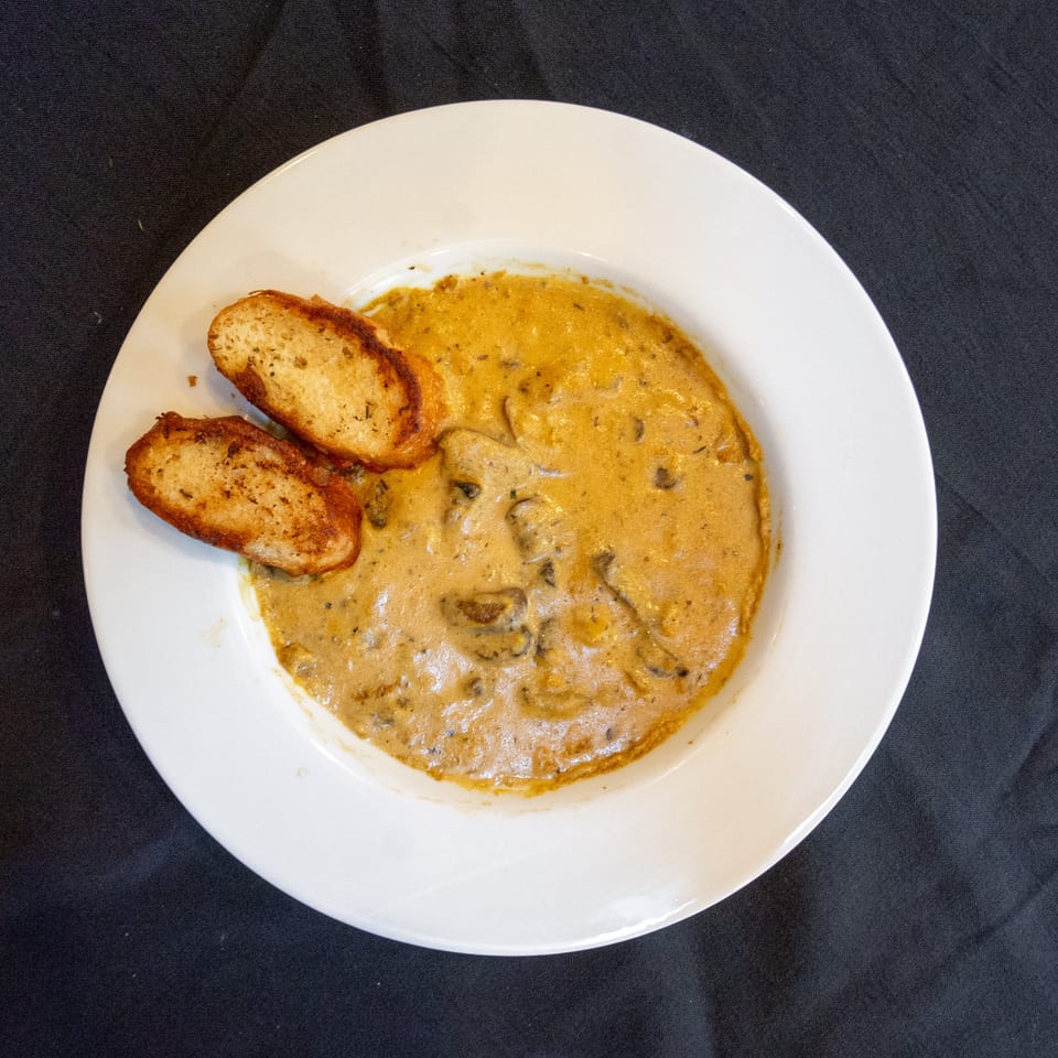Creamy mushroom soup with two pieces of toasted bread on a white plate, against a dark background.
