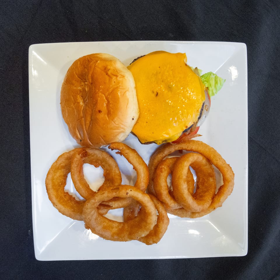 A cheeseburger with lettuce, tomato, and onion rings on a white square plate.