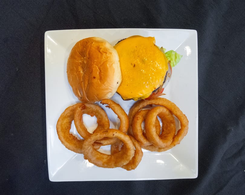 A cheeseburger with lettuce, tomato, and onion rings on a white square plate.