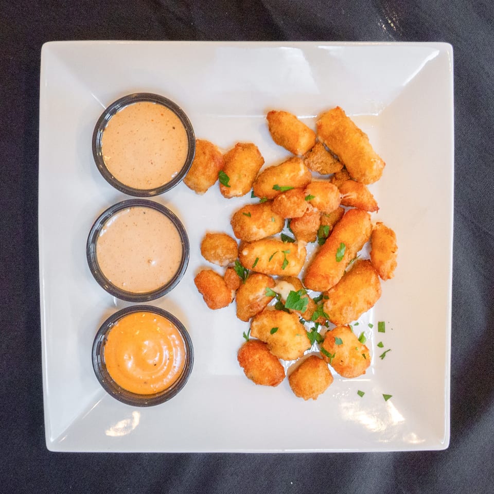 Golden fried cheese curds and mozzarella sticks with three dipping sauces on a white plate.