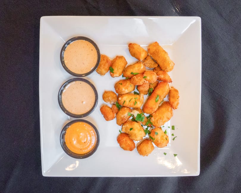Golden fried cheese curds and mozzarella sticks with three dipping sauces on a white plate.