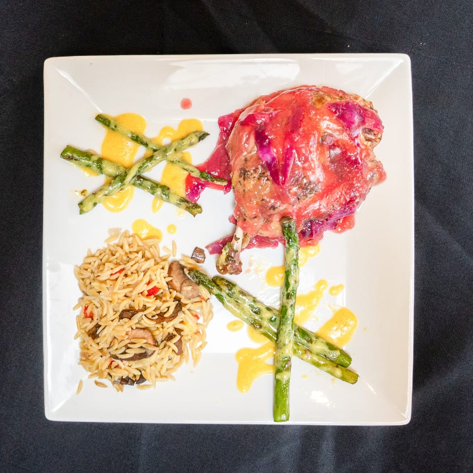 Duck confit with red cabbage, asparagus, and orzo pasta on a white plate.