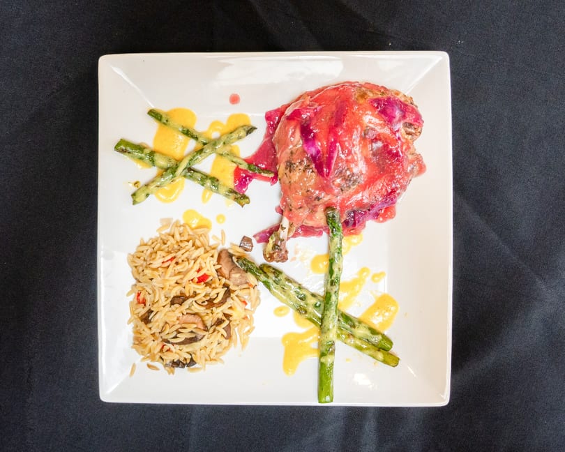 Duck confit with red cabbage, asparagus, and orzo pasta on a white plate.