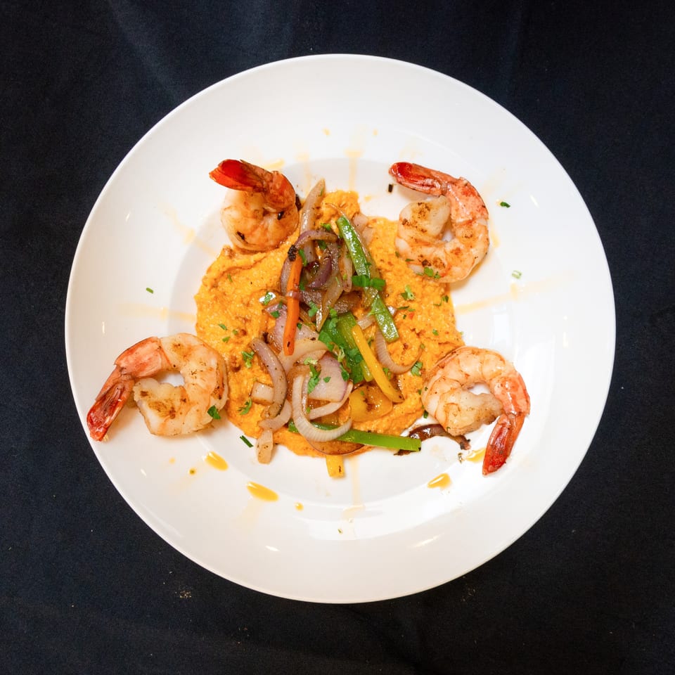 Four grilled shrimp surround a bed of orange puree topped with sautéed onions and peppers.